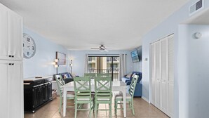 A dining area with a table and chairs, a kitchen with cabinets, and a living area with a sofa and a TV. - Wight Bay 254 by Seaside Vacations & Sales (Ocean City)