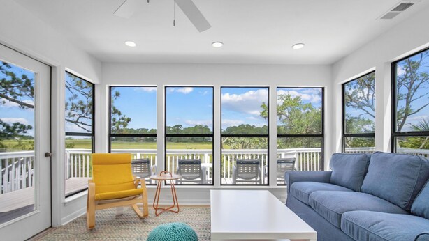 A spacious room with a large window, a yellow chair, a blue sofa, and a white table. - Gorgeous Sunsets and Marsh Views, Pet Friendly, Golf Cart Included (Fripp Island)