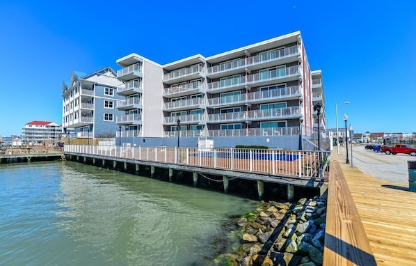 A multi-story hotel with balconies, a wooden boardwalk, and a waterfront view.