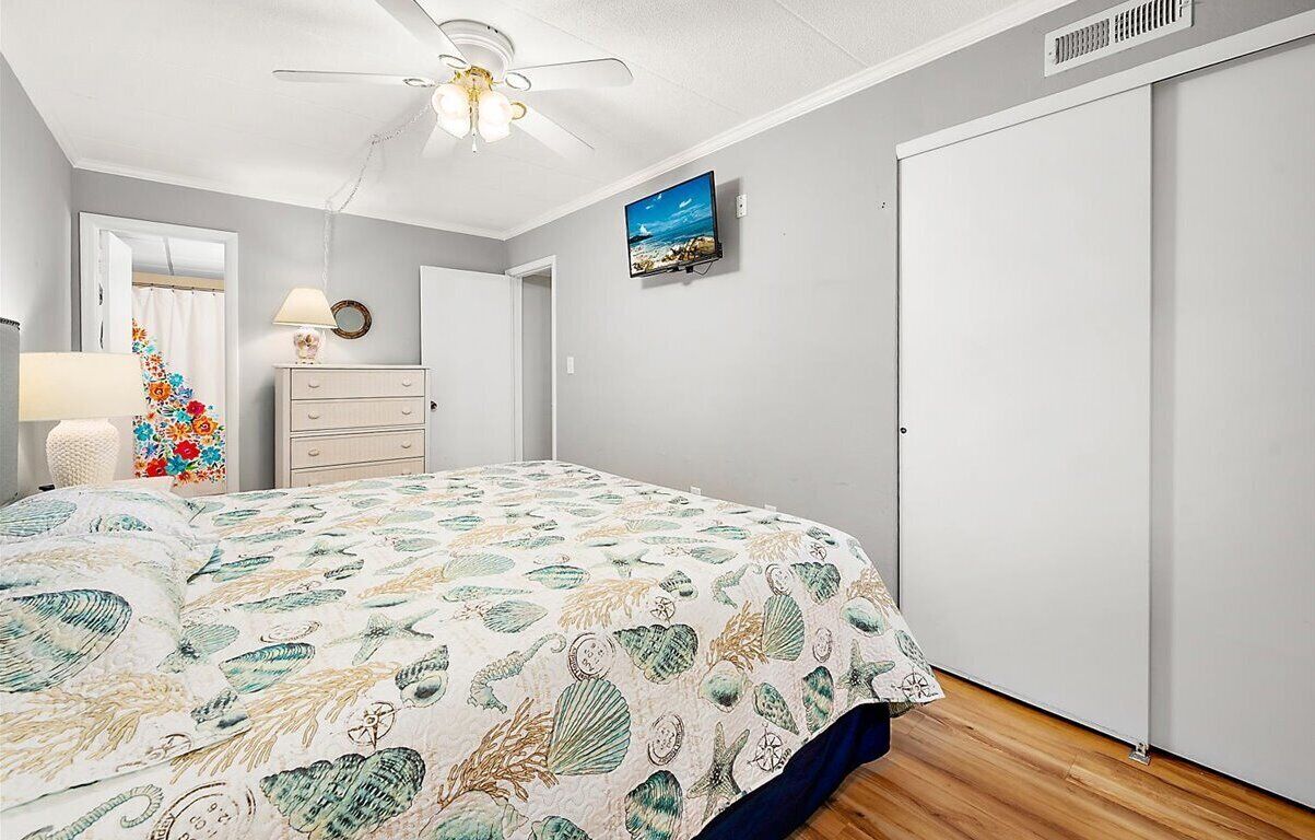A bedroom with a bed, a dresser, a television, and a ceiling fan.