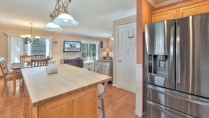 A kitchen with a wooden island, stainless steel refrigerator, and a dining area with chairs and a table. - Harbor View by Seaside Vacations & Sales (Ocean City)