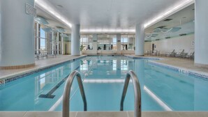 Una piscina interior con agua cristalina, escaleras metálicas y suelo de baldosas.