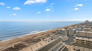 Un hotel frente al mar con varias construcciones, una playa al fondo y un cielo despejado.