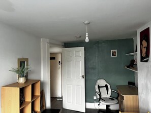 Ein Zimmer mit einer weißen Tür, einem Schreibtisch, einem Stuhl, einem Bücherregal und einer Topfpflanze.