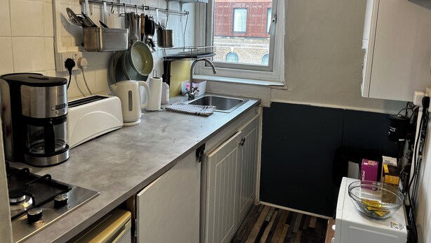 A compact kitchen with a gas stove, coffee maker, and a window with a view of buildings. - 2 Bedroom Basit Flat in Center. (London)