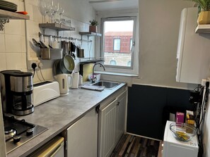 Eine kleine Küche mit Gasherd, Kaffeemaschine und einem Fenster mit Blick auf Gebäude.