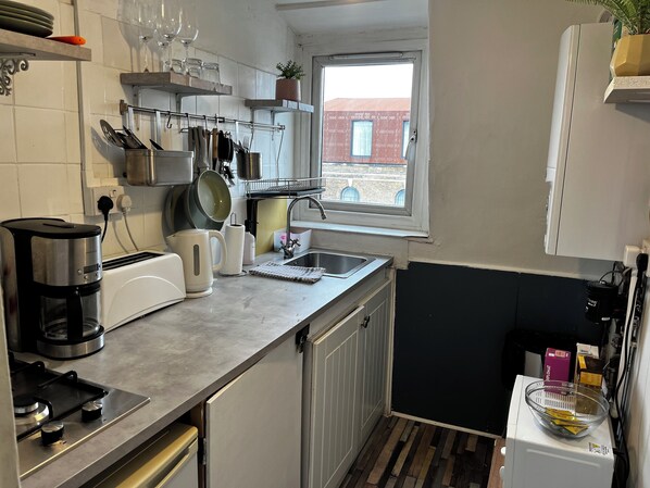 Eine kleine Küche mit Gasherd, Kaffeemaschine und einem Fenster mit Blick auf Gebäude.
