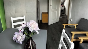 A room with a dining table, a vase with flowers, a grey partition, and a door leading to another room. - 2 Bedroom Basit Flat in Center. (London)