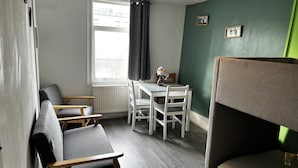 A compact room with a bunk bed, a small table with chairs, a radiator, and a window with curtains. - 2 Bedroom Basit Flat in Center. (London)