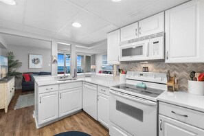 A modern kitchen with white cabinetry, a built-in microwave, a stove, and a large window overlooking a scenic view. - Capri 1702 by Seaside Vacations & Sales (Ocean City)