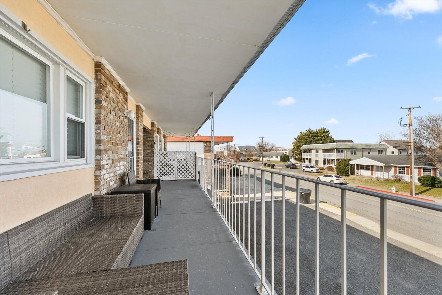 A balcony with a view of a suburban street, a brick wall, and a metal railing.