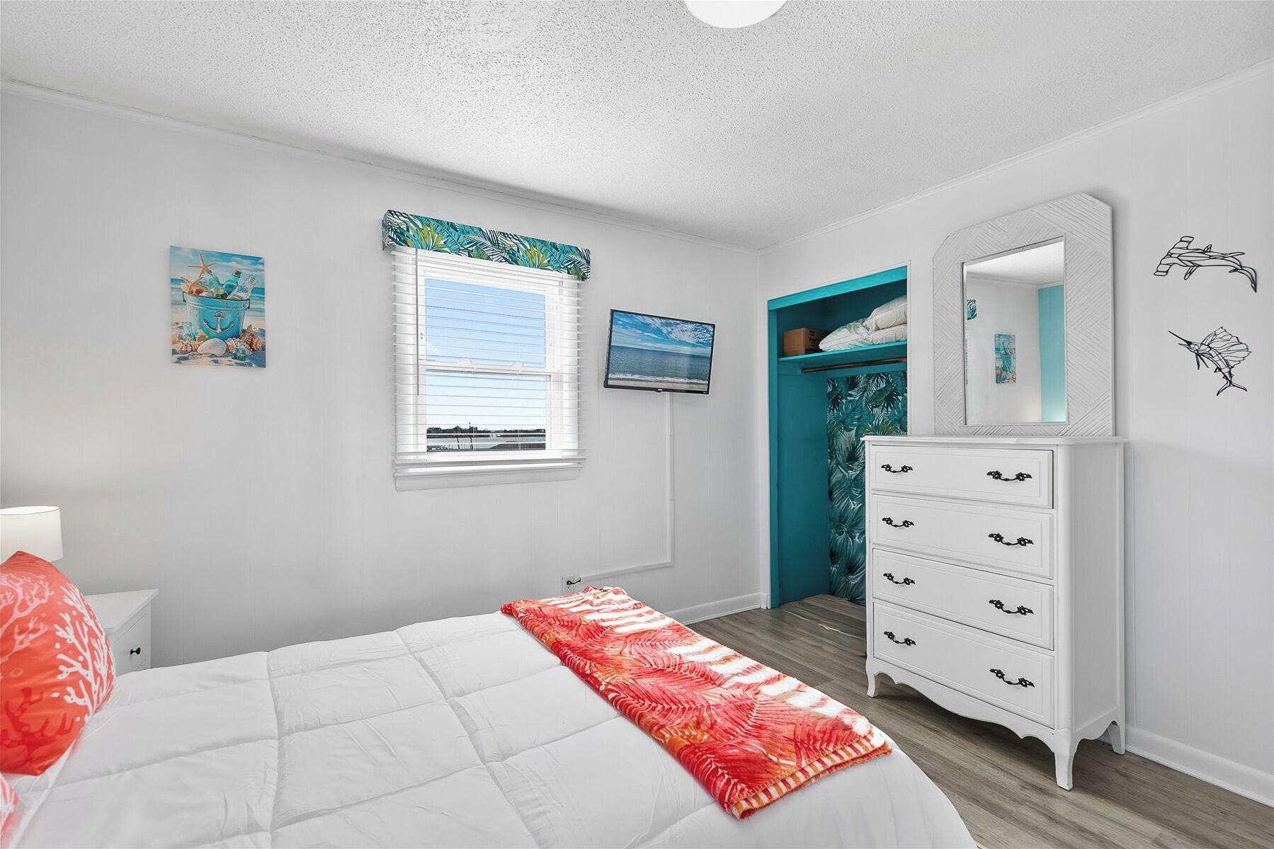 Un dormitorio con cama, cómoda, ventana con persianas, televisor y armario con espejo.