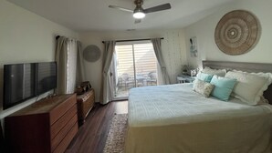 A bedroom with a bed, a TV, a dresser, a ceiling fan, and a view through a sliding door to an outdoor area. - One bedroom Apartment in Rehoboth Beach (Rehoboth Beach)