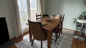 A dining room with a wooden table, four chairs, a chandelier, and a view of the outdoors through large windows. - One bedroom Apartment in Rehoboth Beach (Rehoboth Beach)