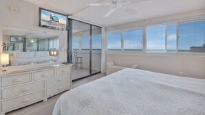 Ein Schlafzimmer mit einem großen Bett, einem Schminktisch, einem Fernseher und einer Glastür zum Balkon.