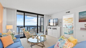 Une chambre d’hôtel moderne dotée d’un balcon, d’un canapé, d’une table ronde en verre et d’un téléviseur.