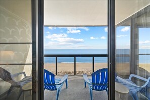 A balcony with a view of the beach, featuring blue chairs and a glass door. - Golden Sands 1115 by Seaside Vacations & Sales (Ocean City)