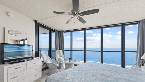 Ein Schlafzimmer mit einem großen Bett, einem Fernseher, einem Deckenventilator und Blick auf den Ozean.