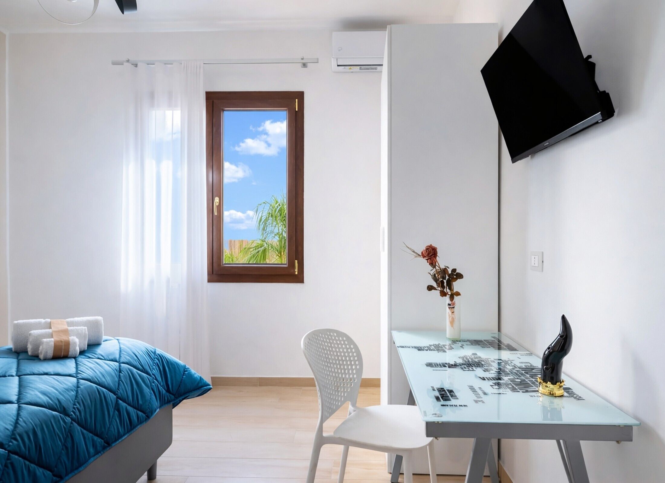 Un dormitorio con cama, escritorio, silla, ventana con vistas y televisor de pared.