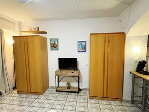 Ein Zimmer mit einem Holzschrank, einem Fernseher auf einem Holztisch und zwei gerahmten Bildern an der Wand.