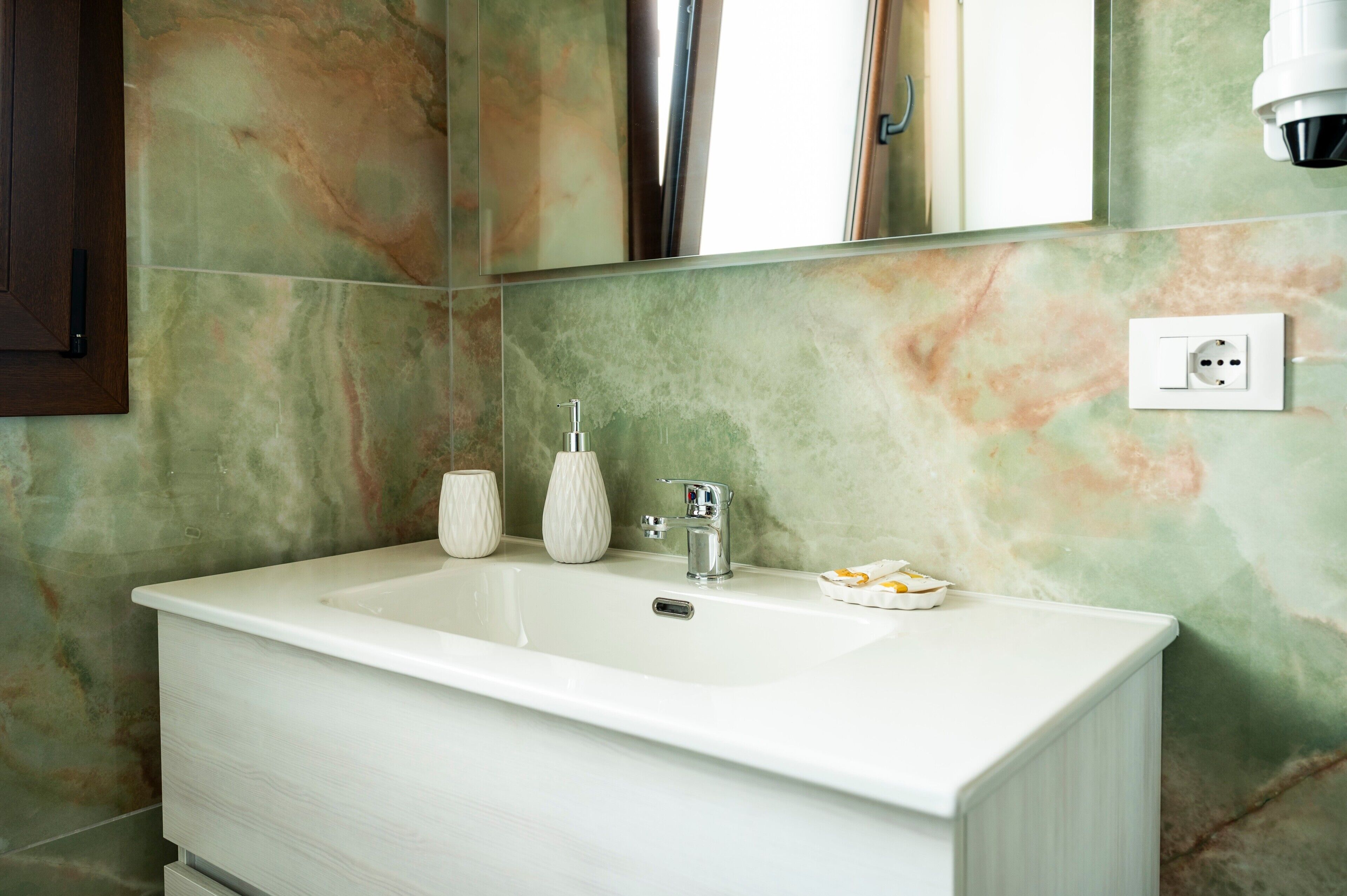 A bathroom with a white sink, a mirror, and a marble wall.