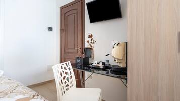 Una habitación de hotel con una cama, un escritorio con cafetera, un televisor y una puerta.