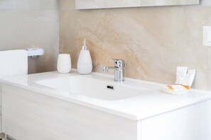 Un baño moderno con un lavamanos blanco, un dispensador de jabón y un perchero para toallas.