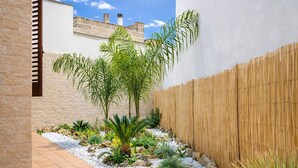 Un jardin où l’on trouve une variété de plantes, une clôture en bambou et un chemin bordé de dalles.