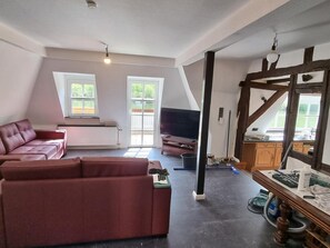 Un salon avec un canapé rouge, un téléviseur et un coin repas comprenant une table et des chaises.