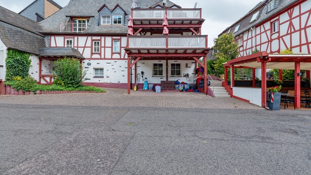 A traditional half-timbered building with a balcony, a covered outdoor seating area, and a paved courtyard. - Top Moselle Apartment: Stunning Panoramic Views (Traben-Trarbach)