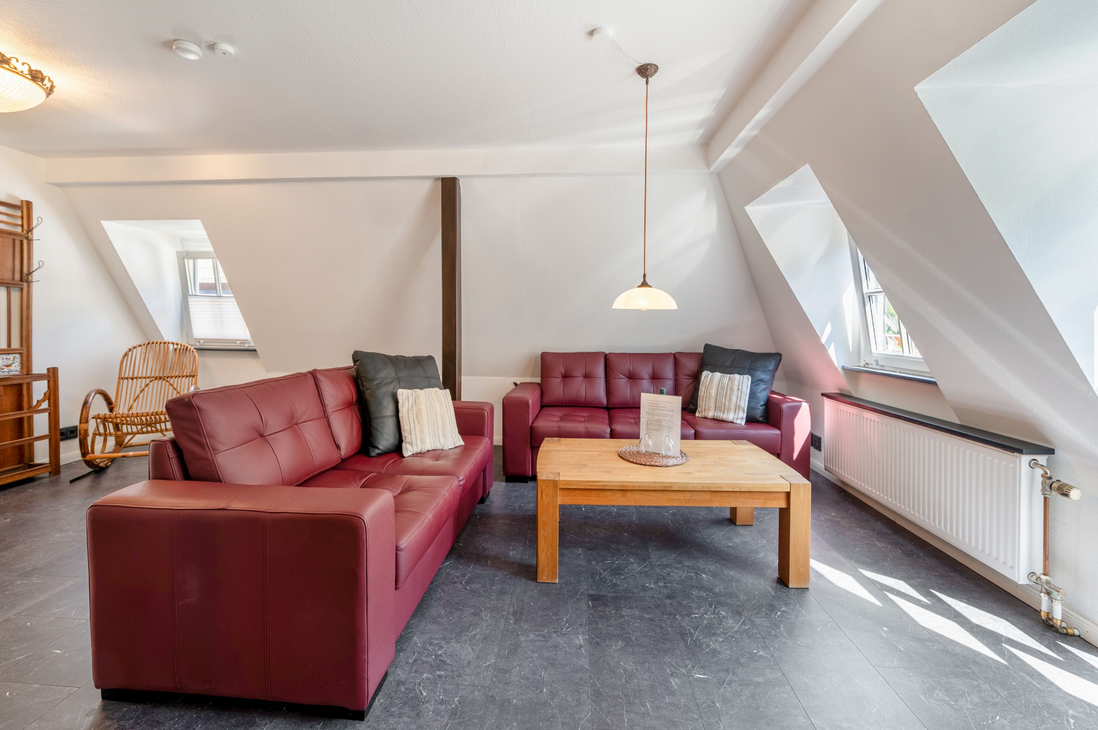 Ein modernes Loft-Apartment mit hohen Decken, freiliegenden Balken und einem geneigten Dach. Es gibt zwei Ledersofas, einen Holztisch und eine hängende Pendelleuchte.