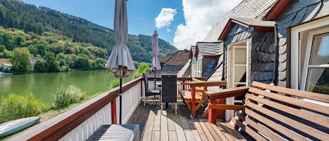 Une terrasse en bois avec des sièges et des parasols, offrant une vue sur un lac et des collines boisées.