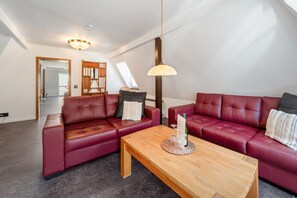 Ein modernes Wohnzimmer mit zwei roten Ledersofas, einem Holztisch und einer Pendelleuchte.