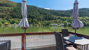 A deck with outdoor seating overlooking a lake, surrounded by forested hills. - Top Moselle Apartment: Stunning Panoramic Views (Traben-Trarbach)
