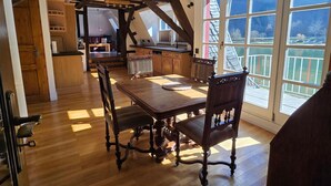 Een eetgedeelte met een houten tafel en stoelen, een keuken op de achtergrond en grote ramen met uitzicht.