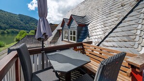 A terrace with a table and chairs, overlooking a lake and forest. - Top Moselle Apartment: Stunning Panoramic Views (Traben-Trarbach)