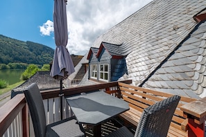 Une terrasse avec une table et des chaises, donnant sur un lac et une forêt.