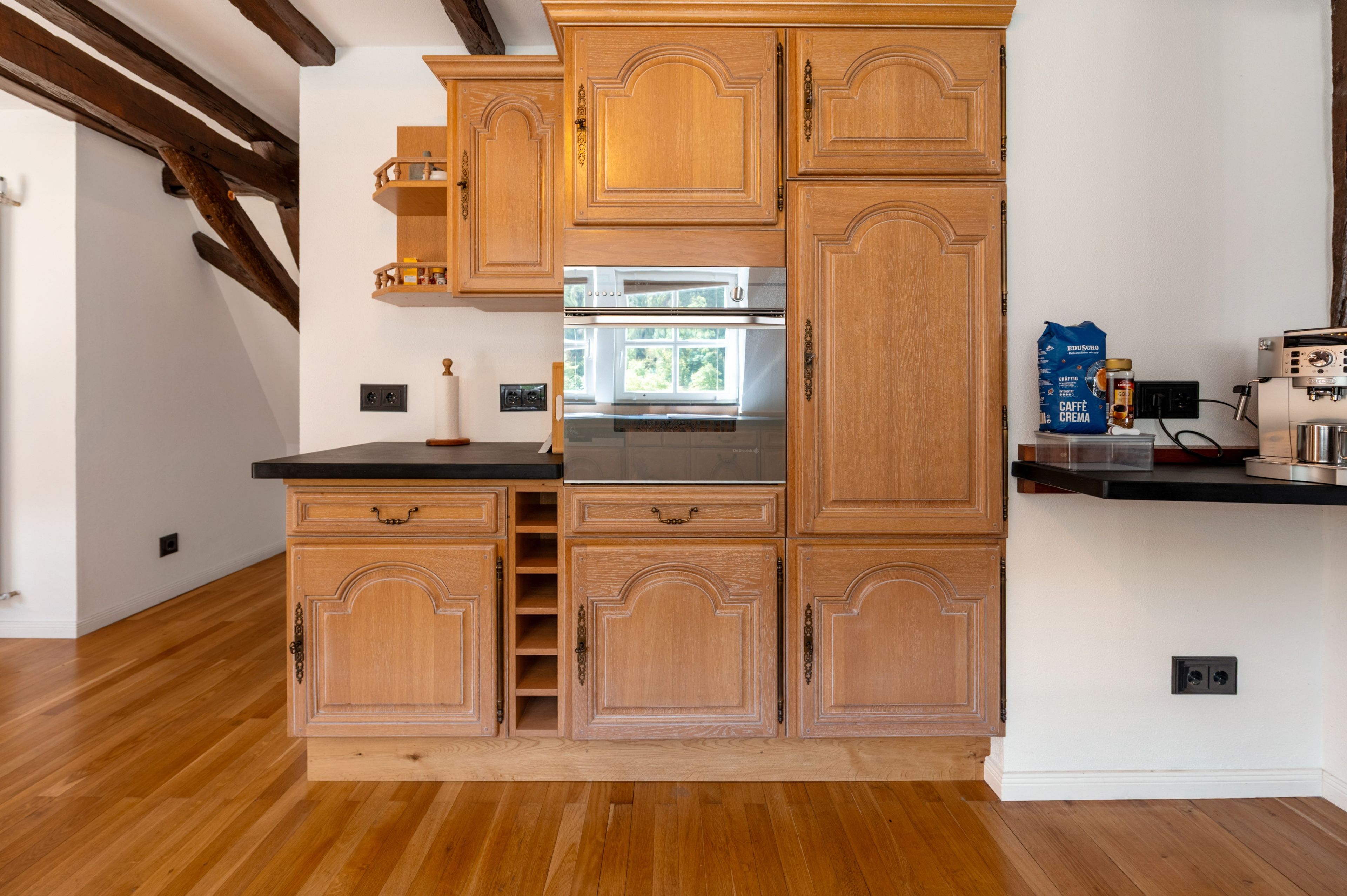 Una cocina con armarios de madera, horno empotrado y cafetera.