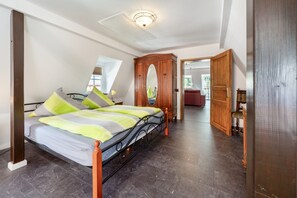 Een slaapkamer met een bed, een houten garderobe, een spiegel en een deur naar een andere kamer.