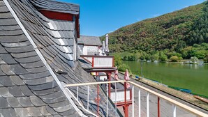 Un bâtiment doté d’un toit en pente, d’un balcon avec une balustrade et offrant une vue sur un lac où naviguent des bateaux.