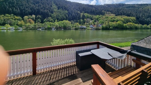 Een terras met uitzicht op een meer, omringd door beboste heuvels.
