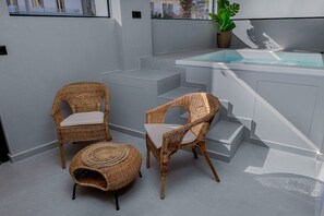 Ein moderner Außenbereich mit zwei Korbstühlen, einem kleinen runden Hocker, einer Whirlwanne mit Glasabdeckung und einem Topfpflanzen.