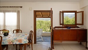 A dining area with a table set for four, a wooden cabinet, and a view of greenery through an open door.