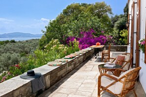 A terrace with wicker furniture, a stone wall, and a view of the sea. - Villa Annelies Pelion (Kato Lechonia)