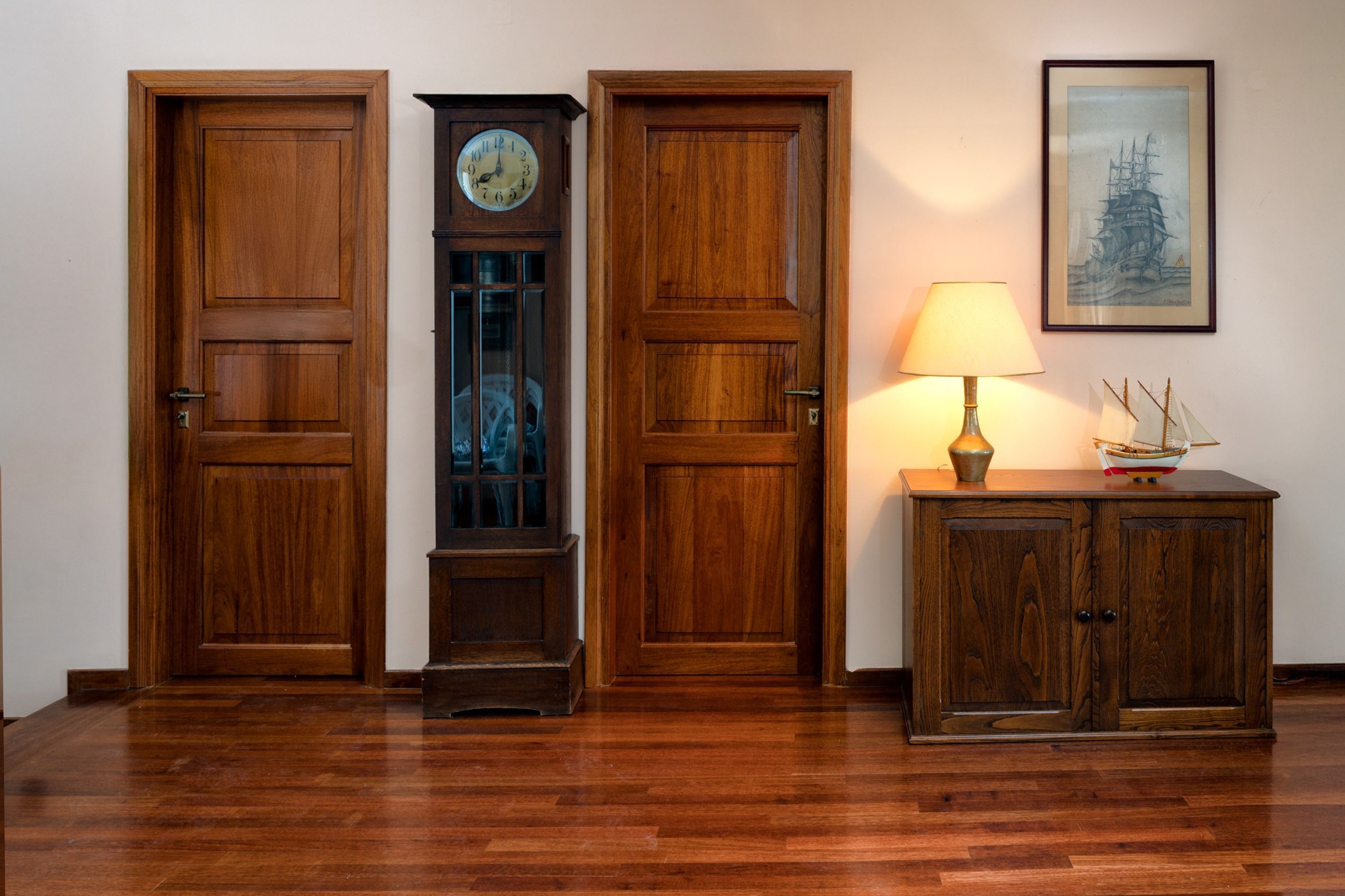 A wooden door, a grandfather clock, a lamp, and a framed picture on a wall.