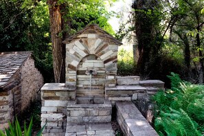 A stone structure with a water spout, surrounded by greenery. - Villa Annelies Pelion (Kato Lechonia)