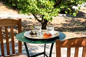 A round table with a green glass top, two glasses of water, a plate with figs and oranges, and a wooden chair. - Villa Annelies Pelion (Kato Lechonia)