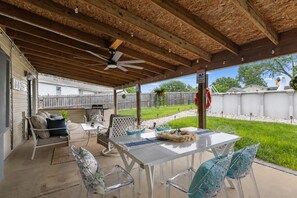 Eine Terrasse im Freien mit Tisch und Stühlen, einem Deckenventilator und Blick auf einen Garten.