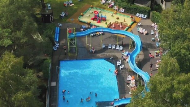 Vista aérea de una zona de piscina con tobogán, área de juegos y vegetación circundante.