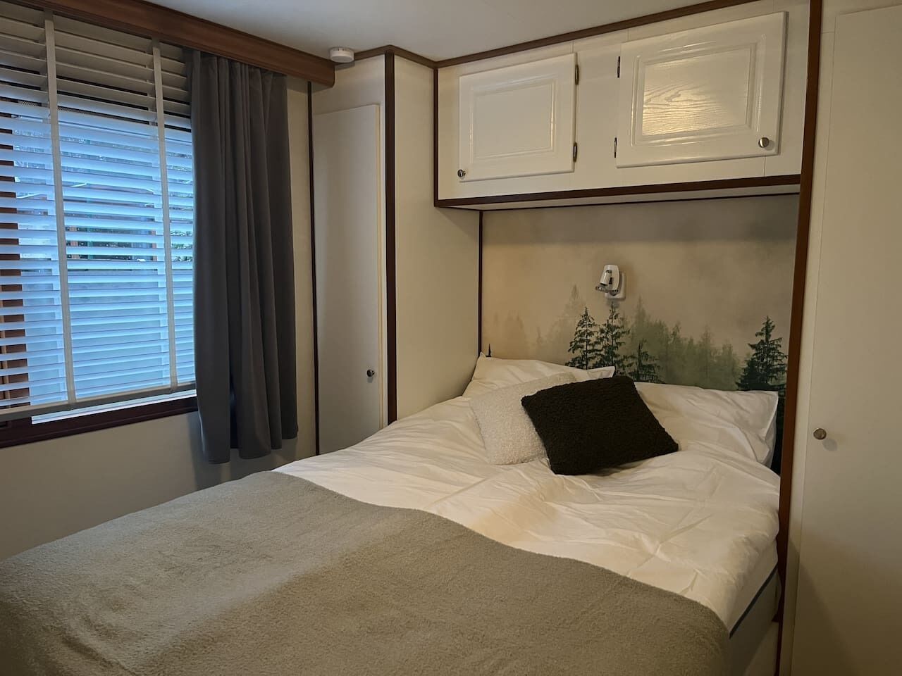 A bedroom with a bed, a window with blinds, and a wall-mounted cabinet.